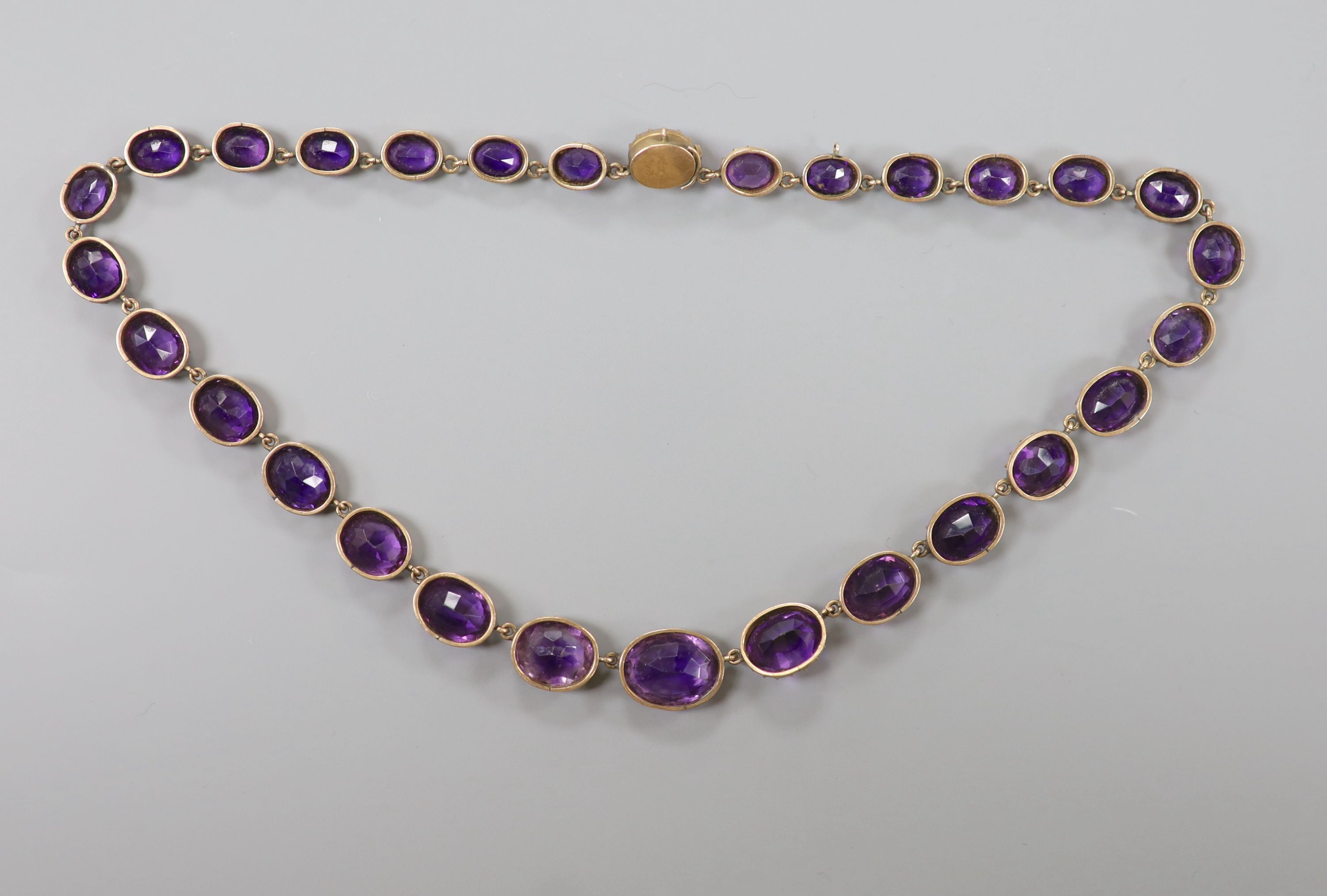 A late Victorian yellow metal and graduated oval cut amethyst set riviere necklace, 39cm, gross weight 37 grams.